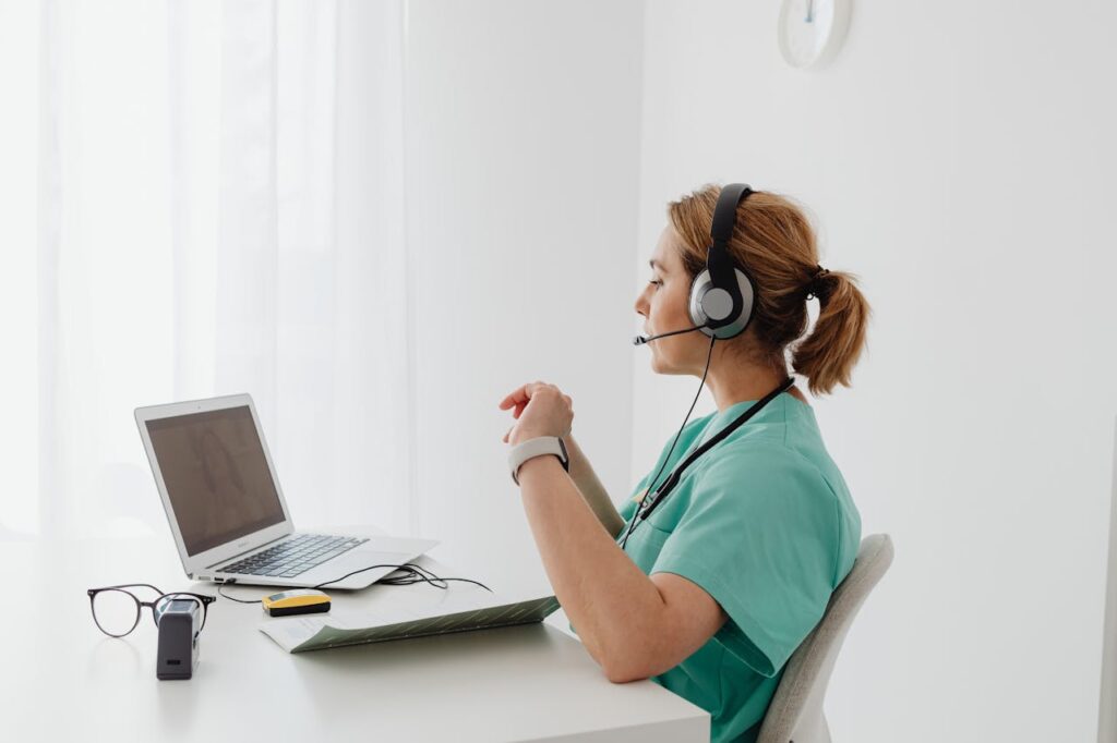 pexels-photo-7195310 A female doctor using a laptop for an online consultation, wearing a headset in a bright office.